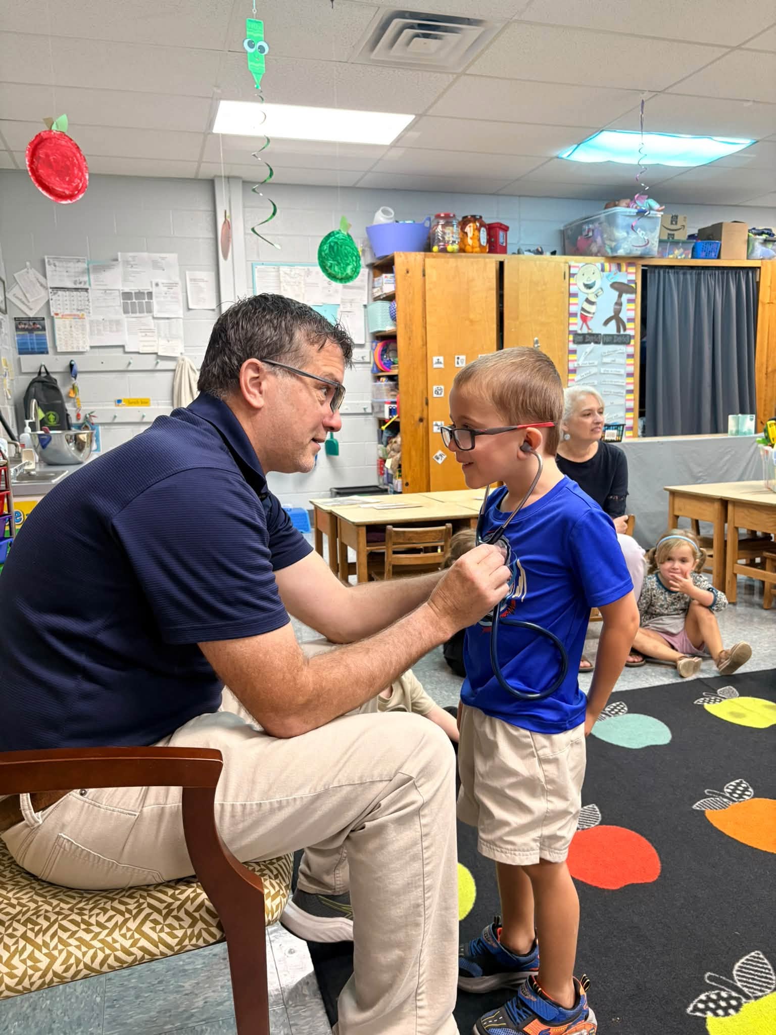 A preschool student explores a stethoscope with an adult in the classroom.
