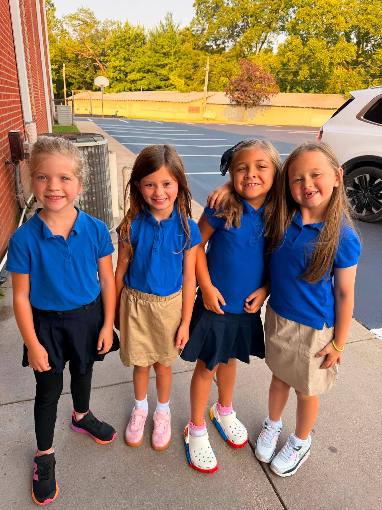 Four students in blue school uniforms stand together outside the school.